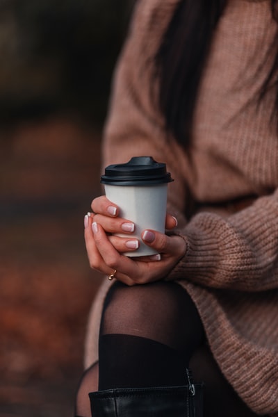 女人棕色毛衣拿着白色的一次性杯子
